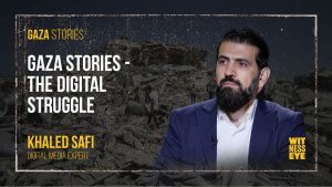 Professor Khaled Safi from Gaza using a laptop amid ruins, symbolizing the digital fight to preserve Palestinian voices.